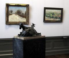 Sculpture of two goats lying down; pastoral paintings in background.