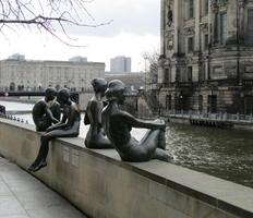 Scultpture: three girls and a boy, sitting on wall overlooking river