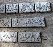 Brick wall with attached pieces of Greek sculpture of men in battle