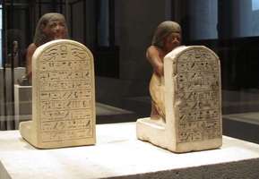 Small statues of two Egyptian scribes seated before steles.