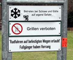 Sign displaying warnings about walking on ice and snow, no grilling, and bicycles being on marked paths only.