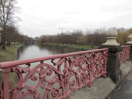 View of river spree from bridge. Reddish metal railing with fleur-de-lis pattern in foreground