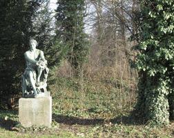 Statue of seated man; statue is on grass near trees