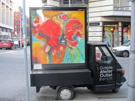 Other side of small truck with advert for Galerie Atelier Outlet; abstract painting of flower on display