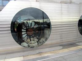 Ruins of old means of transport embedded behind round glass panels at base of statue of horse.