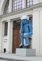 Large wooden sculpture of blue man in front of museum entrance