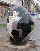 Somewhat irregularly egg-shaped sculpture on street; mostly black with color designs