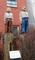 Wooden sculptures of two men with cartoon-like faces atop wooden poles