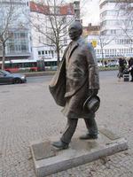 Metal sculpture of Konrad Adenaur, walking and holding hat in hand.