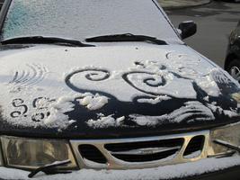 Curlicues drawn in snow on black car hood
