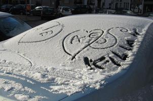 Hearts with initials drawn in snow on car windshield