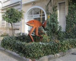Copper-colored statue of fish on human-proportioned legs in front of Horst Dietrich Galerie