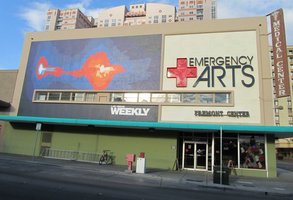 second floor facade; Neon red cross and legend “Emergency Arts”