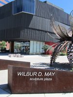 Sign reading “Wilbur D. May Sculpture Plaza&8221; in foreground; museum building in background