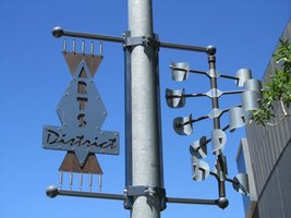 Sculpture on light pole; left half reads “Art District” right half is metal spiral that rotates when wind blows