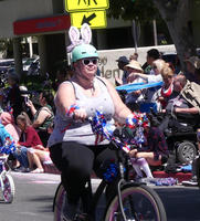 Woman riding bicycle; wearing teal helmet with bunny ears on it.