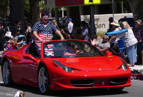 Person in flag-themed outfit riding in red sports car convertible