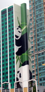 Cylindrical column on side of building painted as a green bamboo tree with pandas climbing it