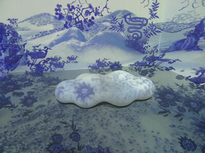 Installation with video that puts blue Chinese style graphics over the walls and a white stone in the foreground.
