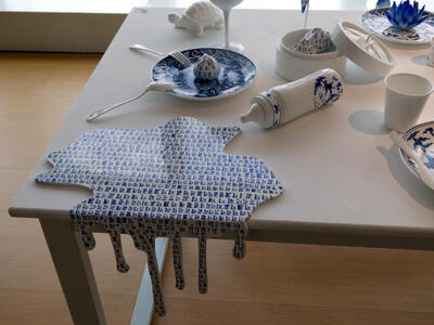 Table with ceramic plates and food, and a bottle that has “spilled” a ceramic spill covered in Chinese-like characters.