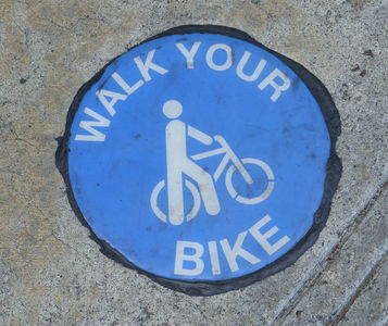 Round blue “walk your bike” sign embedded in sidewalk.