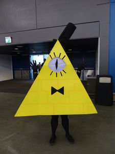 Cosplayer in a one-eyed yellow triangular costume with top hat and bow tie.