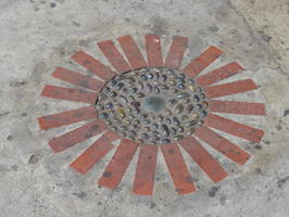 Sidewalk decoration in form of sun; cobblestone in center, painted red rays