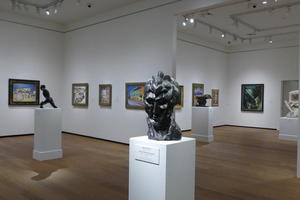 Long shot of gallery with paintings in background and abstract bust of man in foreground