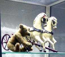 Teddy bear playing horn next to two toy horses