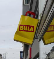Three-dimensional yellow BILLA shopping bag on side of store