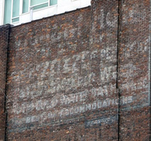 Illegible faded sign on brickwork of building