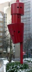 Large sculpture with three red cork-like elements stack one atop the other.