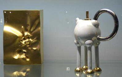 Gold bag on left; teapot with very long legs on right