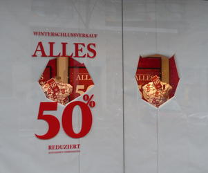 Sign for a sale in windows; windows are covered in paper with holes “torn out” to see merchandise.