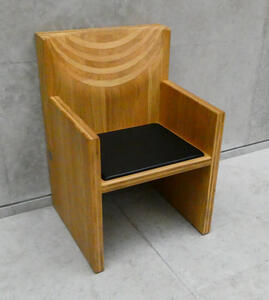 wooden chair w. black seat cushion; back of chair has semi-circular carved areas.