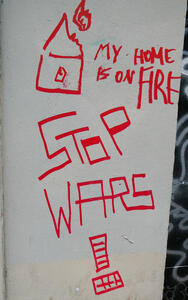 Graffitti showing crude line drawing of burning house: My House is on fire / Stop wars !