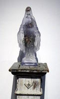 Glass sculpture of Virgin Mary on wooden pedestal.