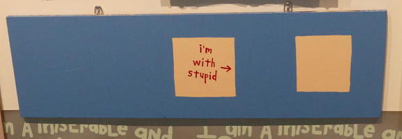 Blue poster with two squares. Left square has arrow pointing to right and words “I’m with stupid” - right square is blank