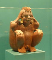 Smiling terra cotta figure sitting on haunches, has gold earrings