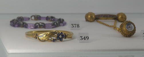 Gold bracelet with blue flowers in front left, purple crystal bracelet in back left, watch pendant on right