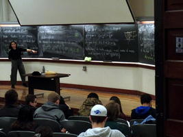 Lecturer in front of multiple chalkboards filled with mathematical symbols