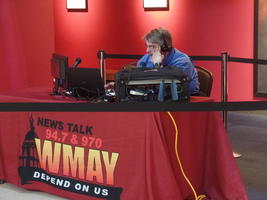 Man in blue shirt in front of microphone and monitors for WMAY radio