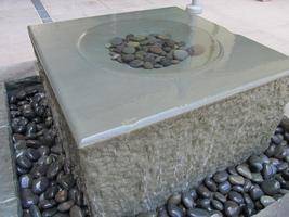 cubical stone fountain with circular depression on top; stones in depression