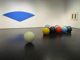Giant billiard balls racked up with cue ball in foreground, blue arc on wall in background