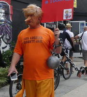 Man made up as Trump; dressed in orange LA County Jail T-shirt with ball & chain
