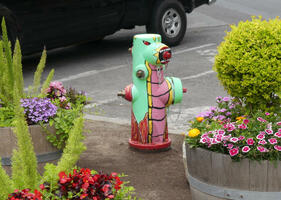 Fire hydrant painted like Godzilla; it is surrounded by planters with flowers