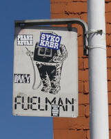 Sign for a gas station: FUELMAN, with logo character having a SYKO KRBR sticker over its head