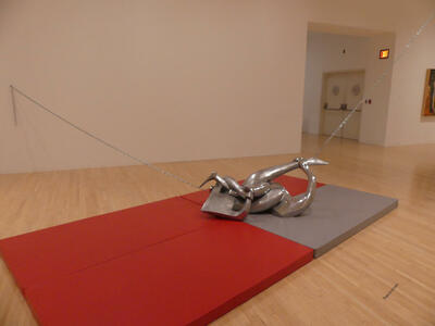 Abstract metal sculpture of intertwined arms, chained to walls, resting on  red and gray exercise mats