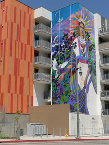 6-story tall mural of latina woman and doves; orange painted wall on building to left