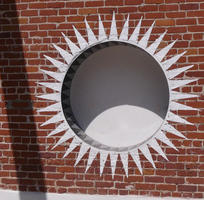 White sunburst pattern around a circular hole in a red brick wall.